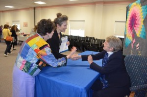 Preparing to sign books at the reception, Lowry shakes hands with Gwynne Morgan (left), Chair of the West Roxbury Reads Committee, and Sheila Scott, Branch Librarian.